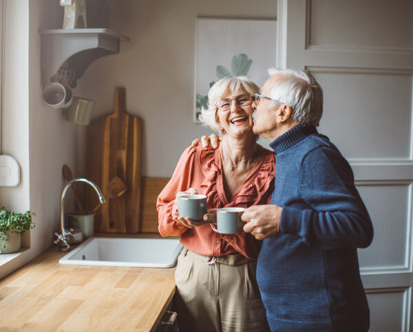 Senior couple at a sink drinking from coffee mugs.